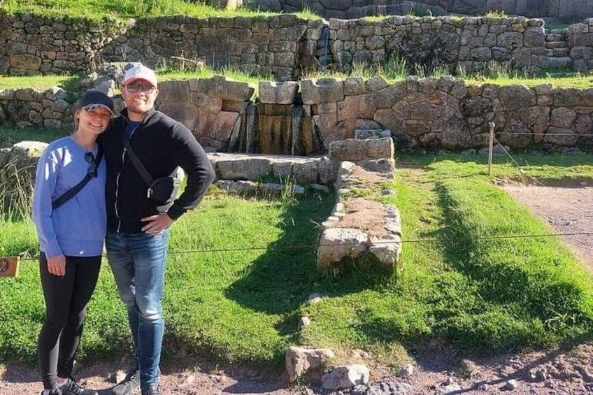Zwei Personen vor alten Steingebäuden, im Hintergrund eine Wiese und eine Steinmauer. 4