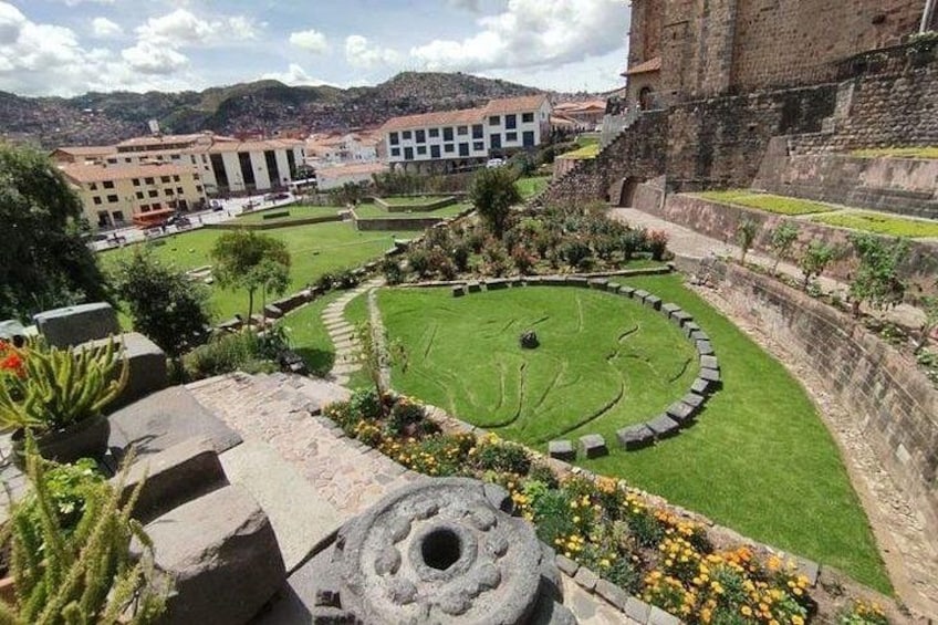 Ein historischer Innenhof mit einem kreisförmigen Garten, Steinmauern und umgebenden Gebäuden. 2