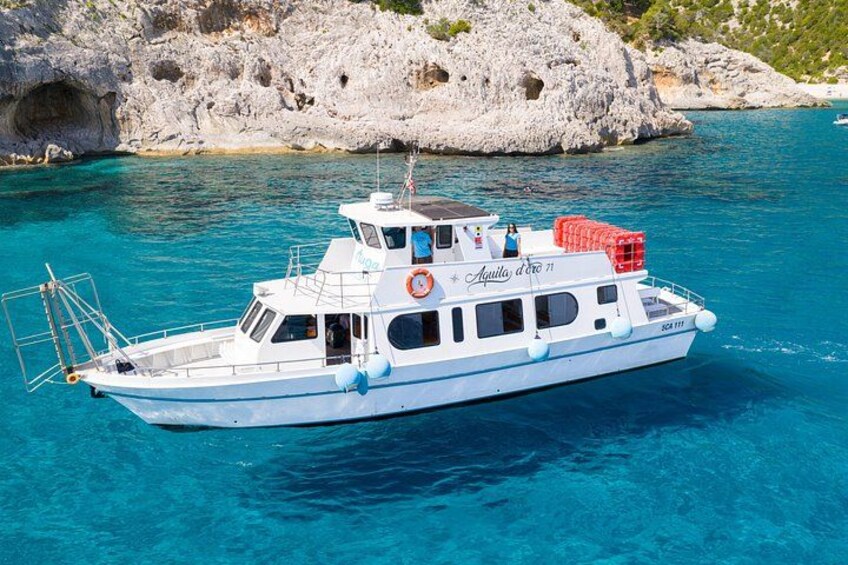 A white boat named 'Aquila d'Oro' on clear blue water with rocky cliffs in the background. 1