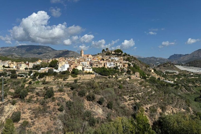 A coastal town with buildings on a hillside, a river, and mountains in the background. 1