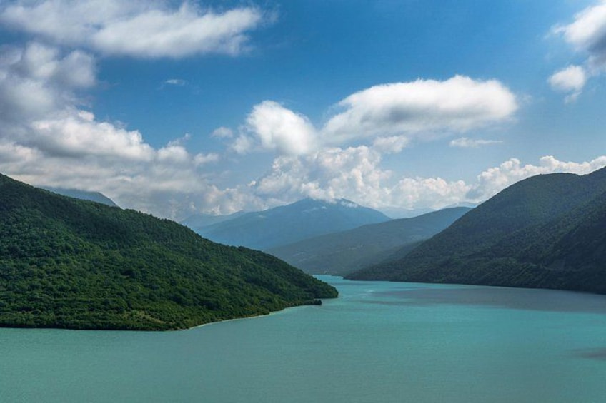 Een turquoise meer, omgeven door weelderige groene heuvels en bergen, onder een gedeeltelijk bewolkte lucht. 2