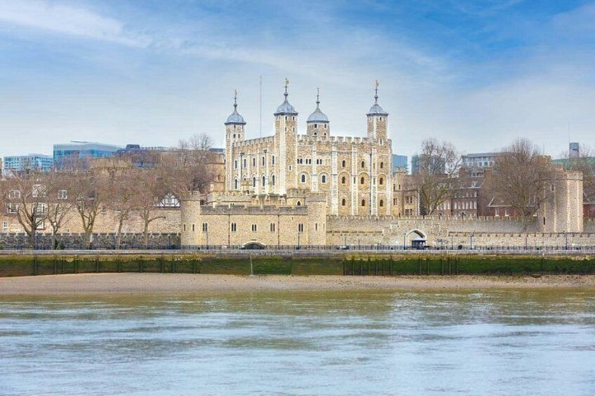 A historic building with multiple towers, a river in the foreground, and modern buildings in the background. 2