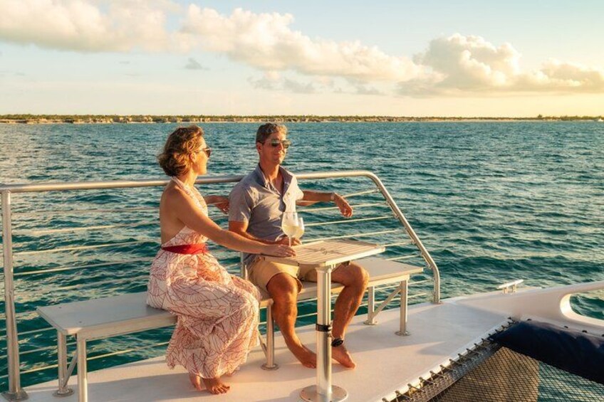 Two people sitting at a table on a boat with a view of the ocean and a distant shoreline. 3