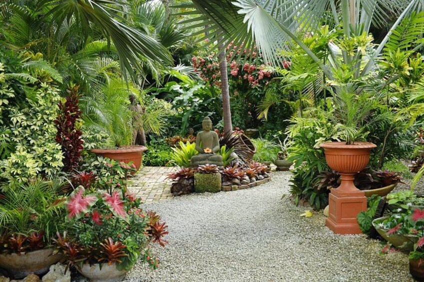 A garden with various plants, a Buddha statue, and a gravel path. 5