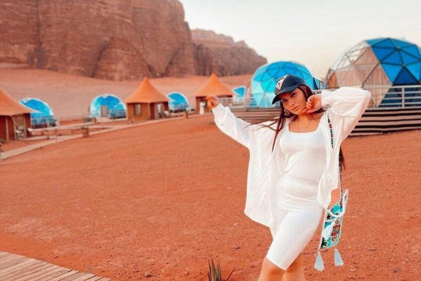 A desert landscape with red soil, a person in white attire, and blue-domed structures in the background. 5