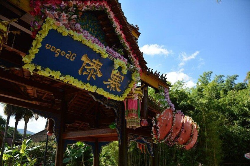 A traditional structure with a blue signboard, surrounded by lush greenery and a clear sky. 2