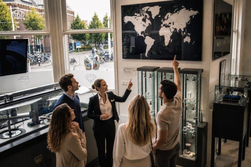 A group of people in a room with a large world map on the wall, a glass display case, and a window with a view of the street outside. 4