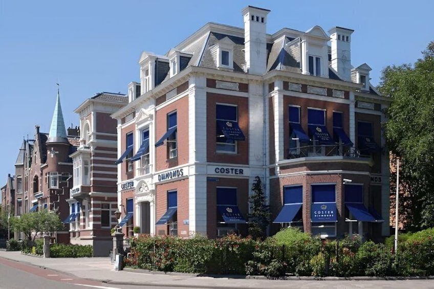 A historic building with 'COSTER' and 'DIAMONDS' signage, surrounded by lush greenery. 2