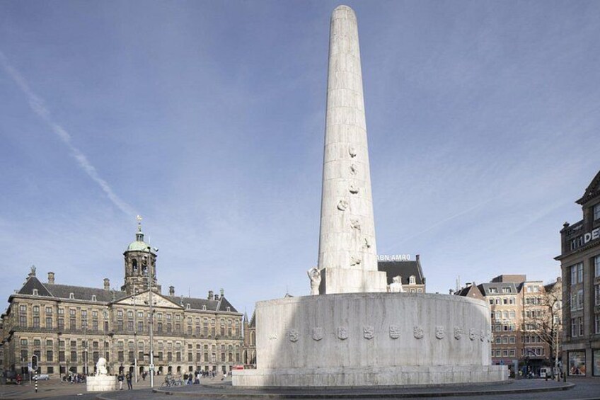 A tall monument with inscriptions, a historic building with a tower, and a clear blue sky. 3