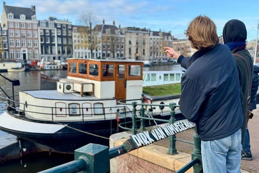 A person pointing at a boat docked in a canal with historic buildings in the background. 4