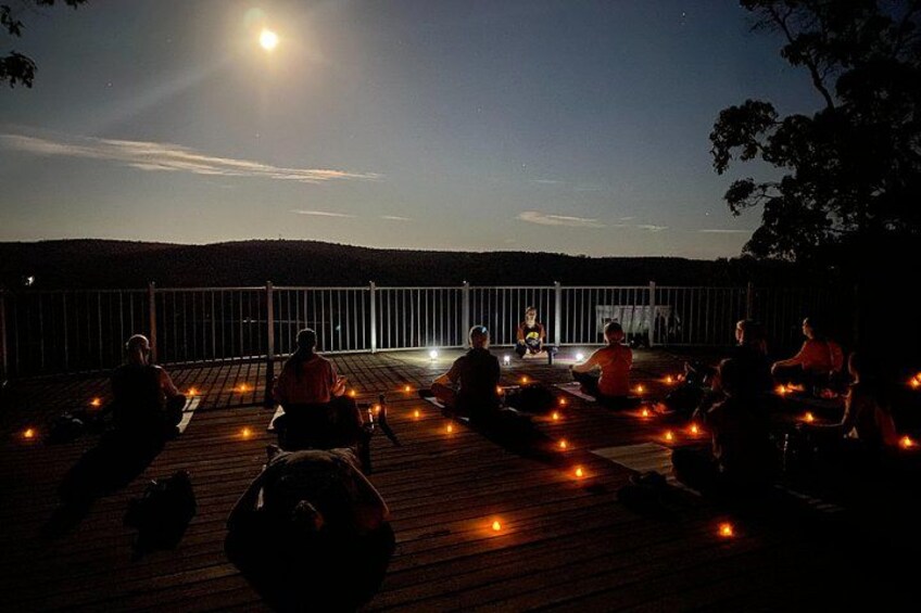 A group of people sitting on a wooden deck outdoors at night with a full moon in the sky. 1