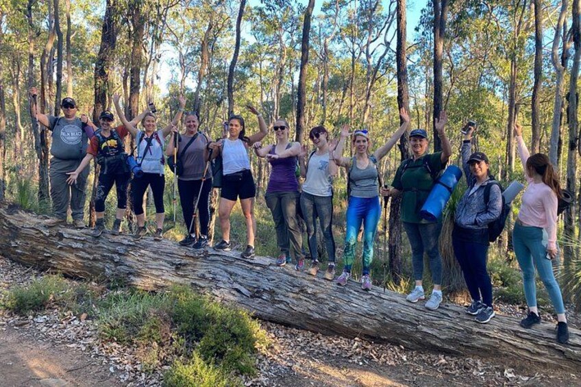 A group of people standing on a fallen log in a forest. 2