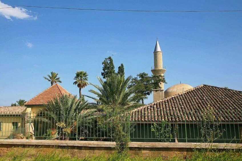 A mosque with a minaret and dome, surrounded by palm trees and a fence. 2