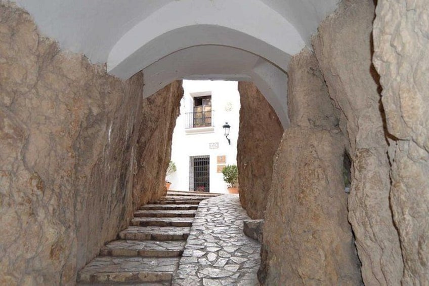 A stone staircase leading to a white building with a balcony, framed by large rock walls. 5