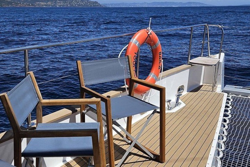 A boat deck with wooden chairs, a life buoy, and a railing. 5