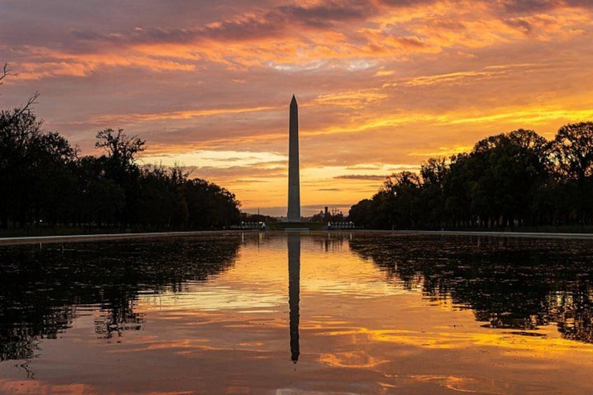 Un coucher de soleil avec le reflet d’un monument imposant dans une étendue d’eau, le tout entouré d’arbres. 1