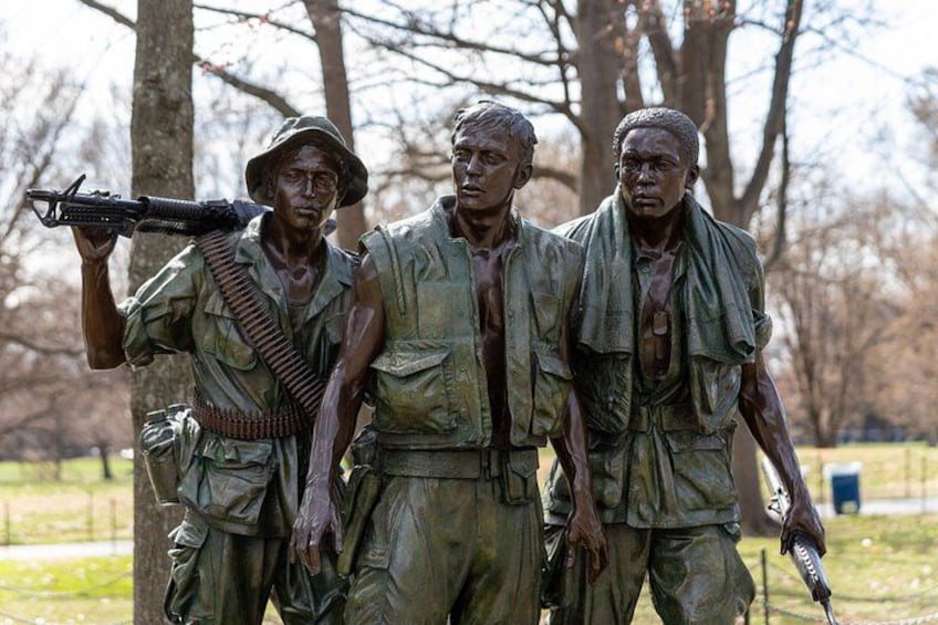 Une statue en bronze représentant des soldats en uniforme, armés de fusils, qui est installée dans un parc arboré et verdoyant. 2