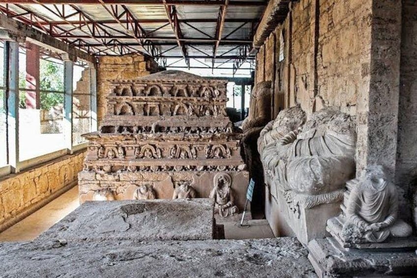 An ancient stone structure with intricate carvings, a seated statue, and a partially visible inscription. 5