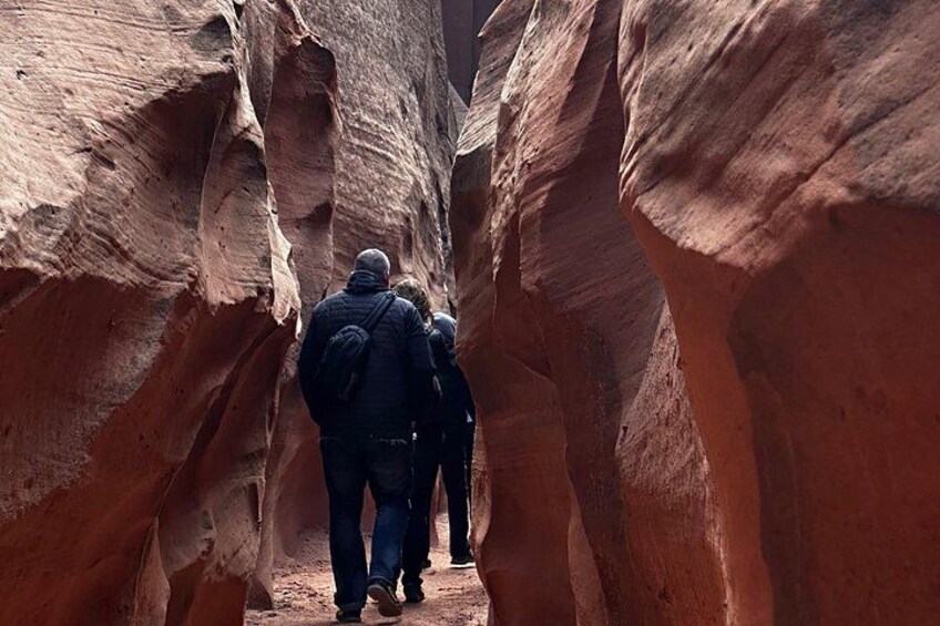A narrow canyon with red rock walls and a group of people hiking through it. 3