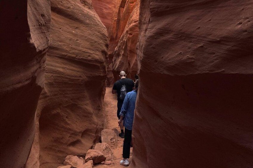 A narrow canyon with red rock walls and two people hiking. 5