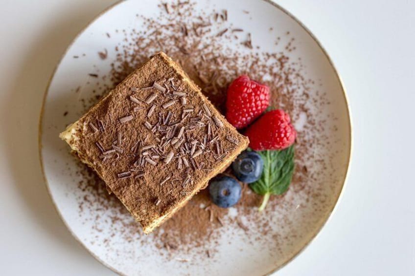 Una porción de tiramisú en un plato con virutas de chocolate, fresas y arándanos. 2