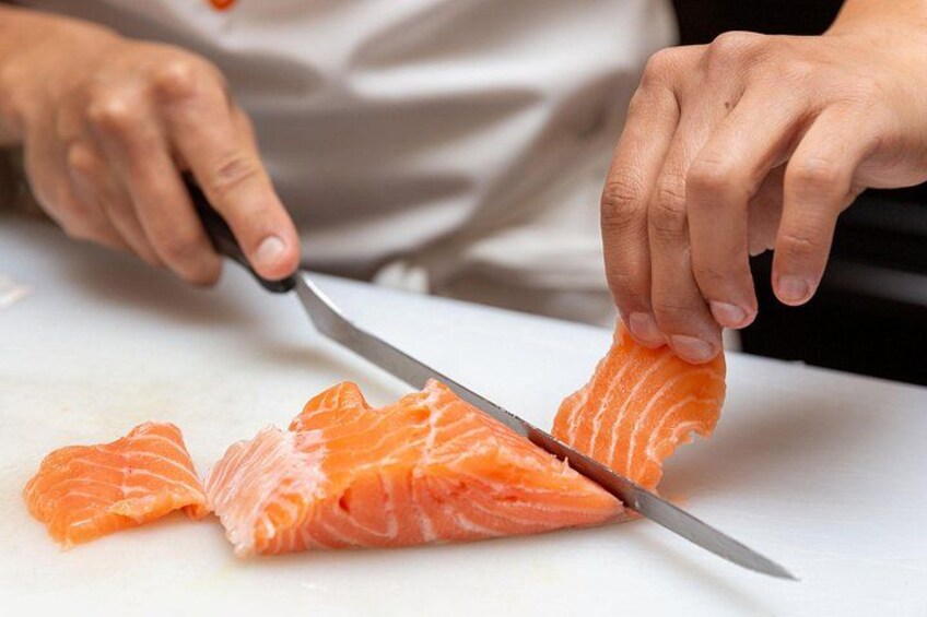 A person slicing salmon on a white cutting board. 2