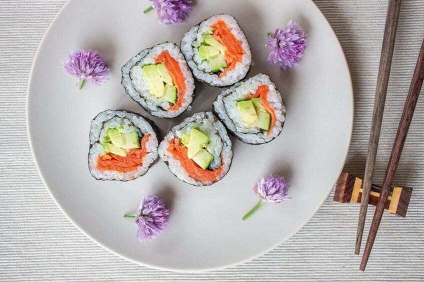 A plate of sushi rolls with avocado and salmon, accompanied by purple flowers and chopsticks. 3