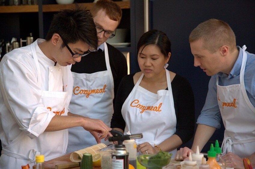 Four people wearing aprons with the word 'Cozymail' on them, working together at a kitchen counter with various food items and cooking utensils. 2