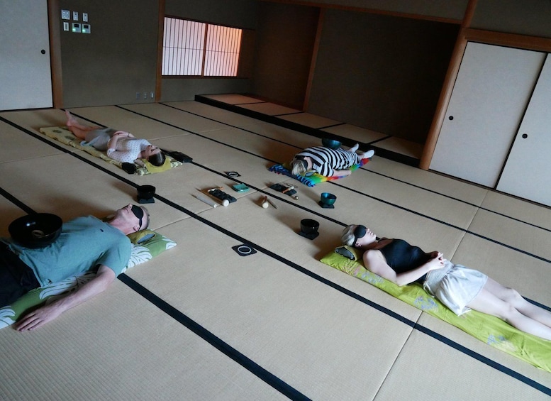People lying on tatami mats in a room with sliding doors and a window with vertical blinds. 3