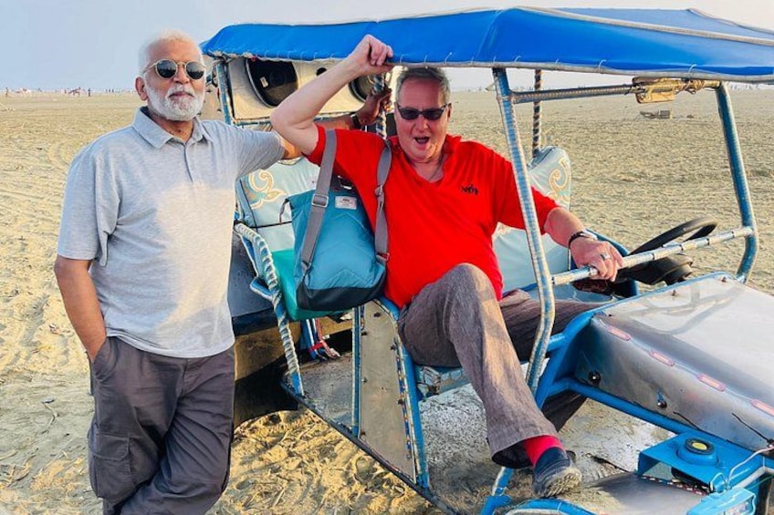 A man in a red shirt sitting in a blue golf cart on a sandy beach. 2