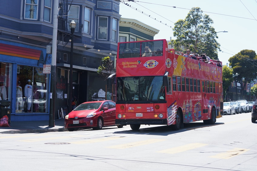 A red double-decker bus with passengers on top, driving on a city street. 1