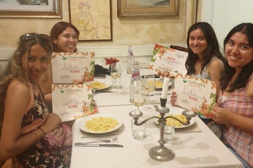 Four people sitting at a table with plates of food, holding certificates. 3