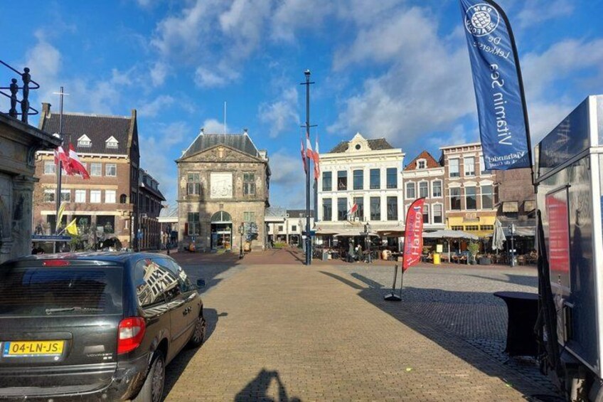 A cobblestone street with historic buildings, a parked car, and flags. 4