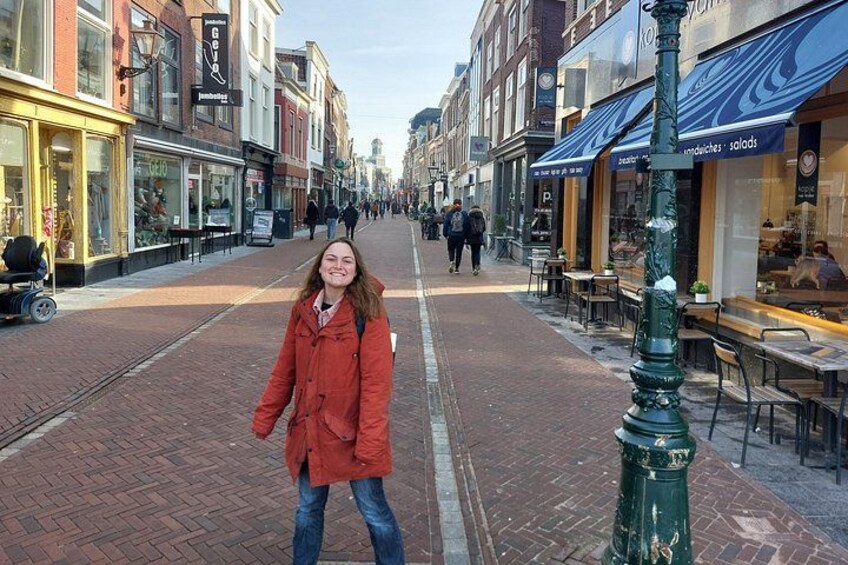 A person in a red coat on a brick-paved street with shops and outdoor seating. 3