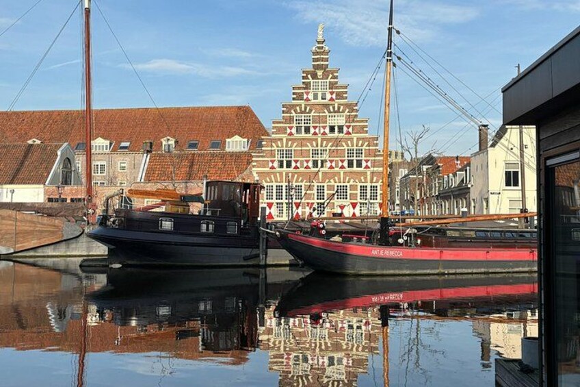 A canal with two boats, a building with a red and white facade, and a reflection of the scene. 2