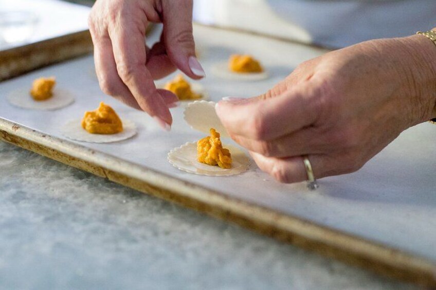 Hands placing a dollop of yellow substance on a round, white object on a baking tray. 2