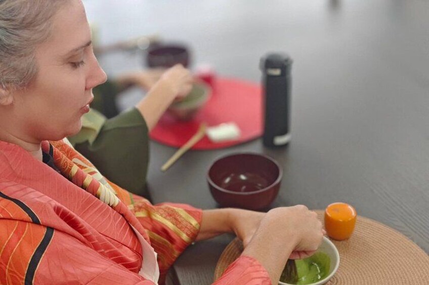 Una persona vestida con un atuendo rojo y amarillo prepara comida con palillos, un tazón y un pequeño recipiente naranja sobre una mesa. 5