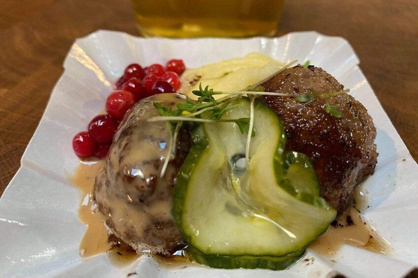 A plate of food with a meat dish, a slice of cucumber, red berries, and a garnish. 4