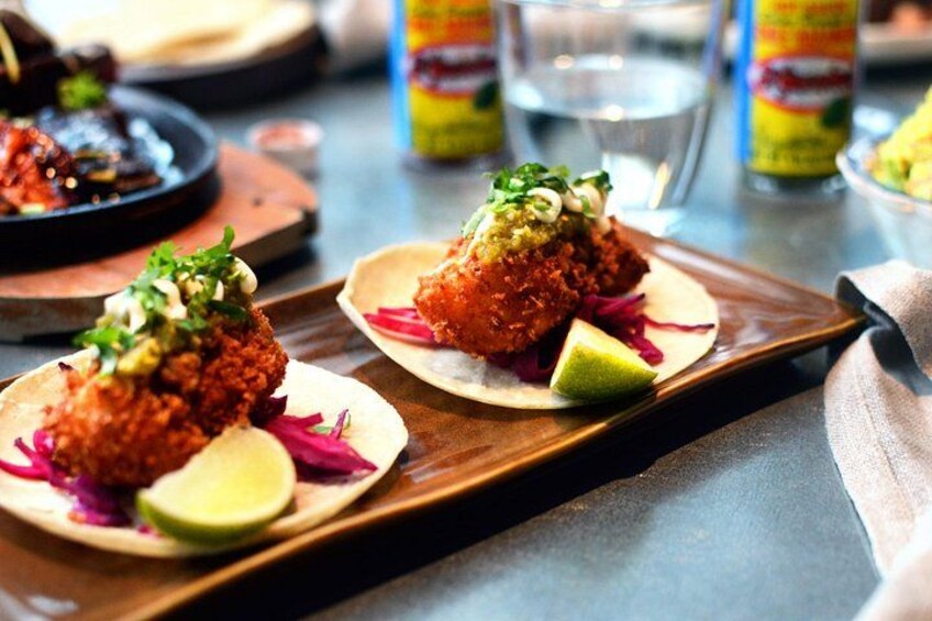 Two tacos with a red sauce, lime wedges, and a green garnish on a wooden board. 2