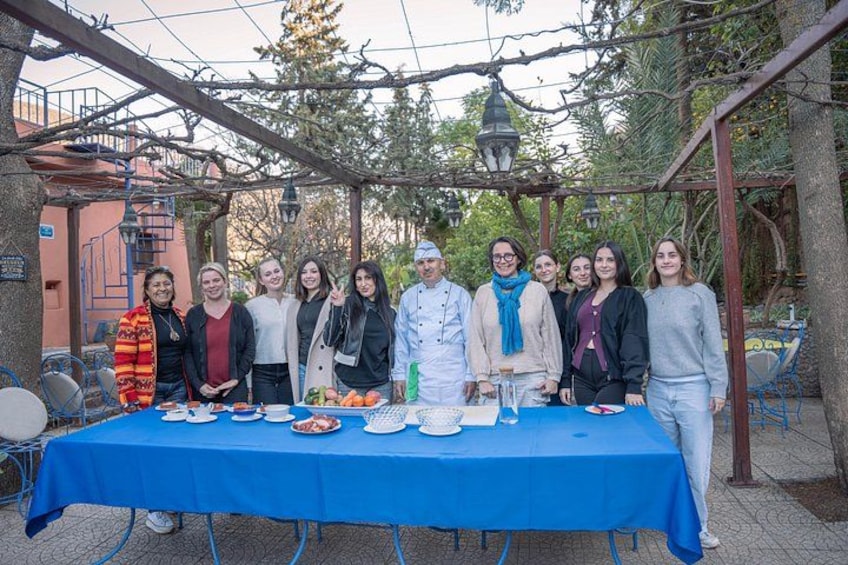 A group of people standing in front of a table with food and drinks, under a pergola with hanging lights. 1