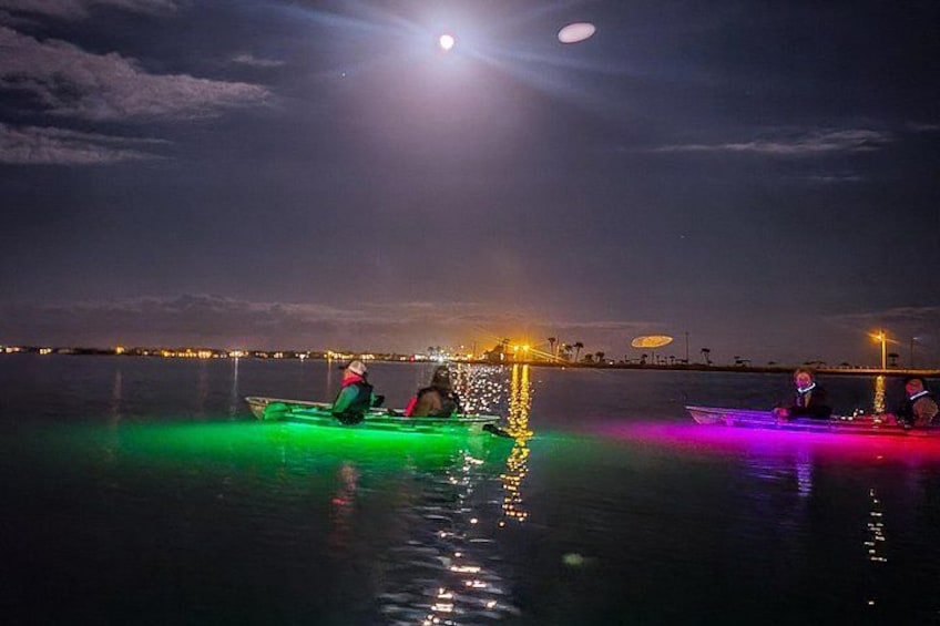 Escena nocturna con personas haciendo kayak en un cuerpo de agua, iluminada por luces de colores. 4