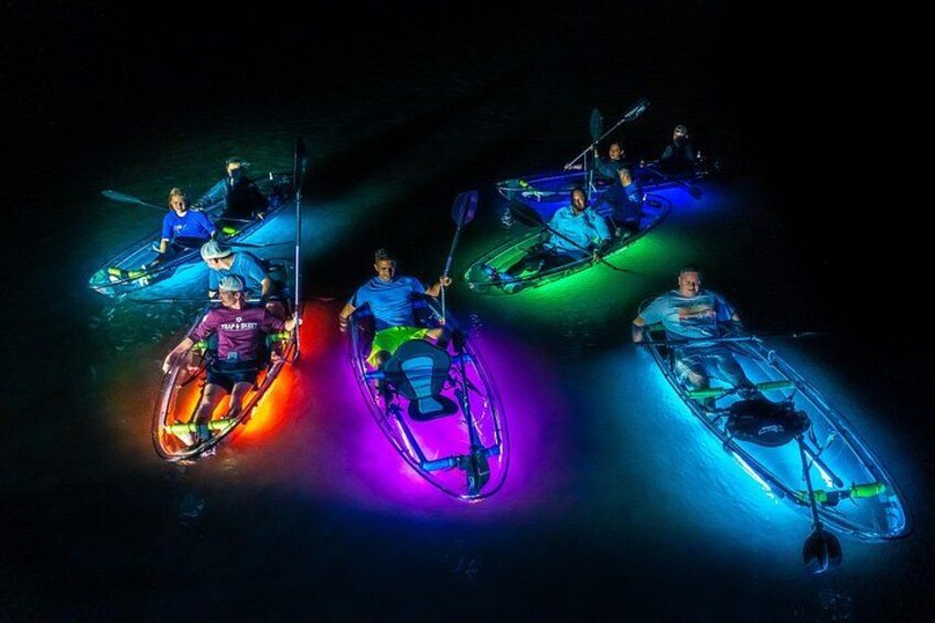 Three kayaks with colorful lights, people paddling, and a dark background. 2