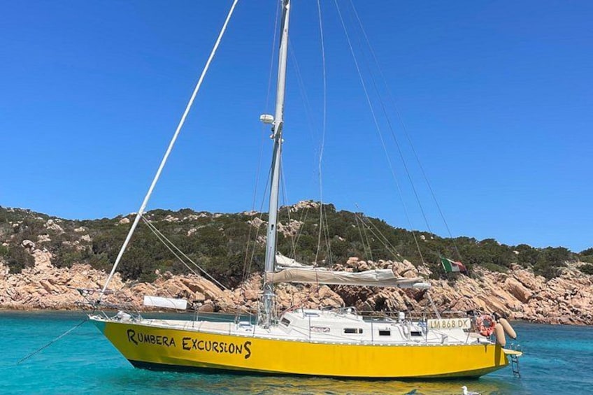 A yellow boat named 'Rumbra Excursions' with a rocky shoreline and clear blue water in the background. 1