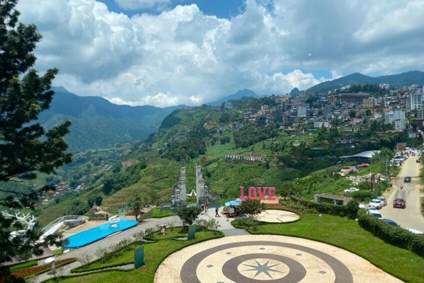 Un paisaje montañoso con una piscina, un monumento con la palabra 'LOVE' y un camino que lleva a un pueblo. 5