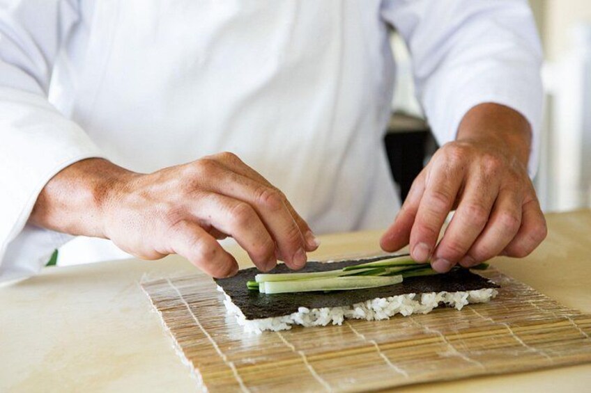 A person preparing sushi on a bamboo mat. 3