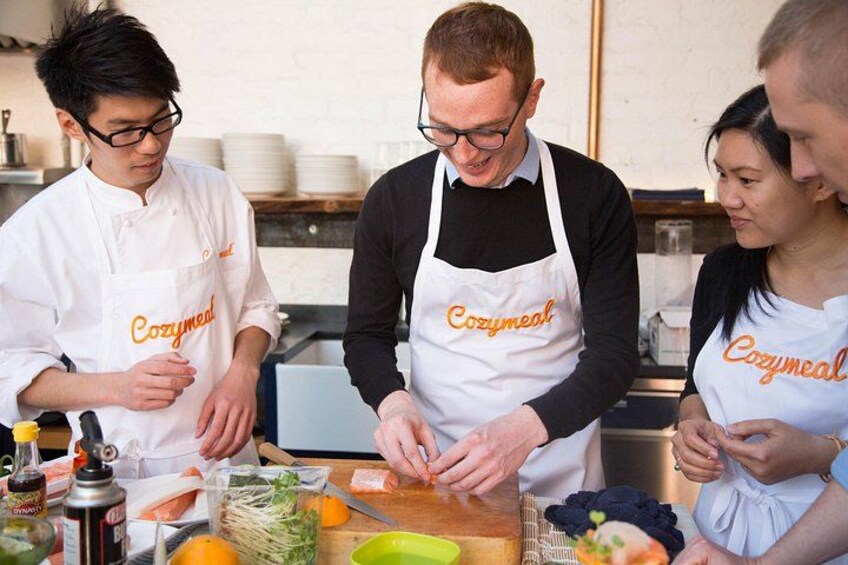 Three people wearing aprons with 'Cozymail' printed on them, preparing food on a wooden table with various ingredients and kitchen tools. 1