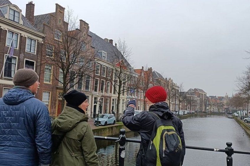 A canal with buildings on either side, a person taking a photo, and another person looking at the scene. 1