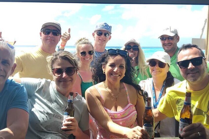 A group of people on a boat with bottles in hand, a clear sky, and the ocean in the background. 1