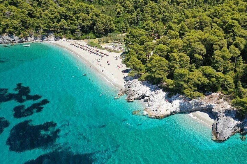 An aerial view of a turquoise beach with a forested area and a rocky shoreline. 5