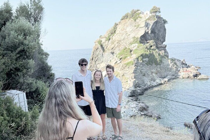 A rocky coastline with a clear sky, a person taking a photo, and a person in a white shirt. 3